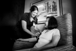 A healthcare worker, supported by corporate sponsors, checks the blood pressure of a seated woman. Both are smiling in a room with a framed painting on the wall, showcasing how community and sponsorships enhance well-being initiatives.