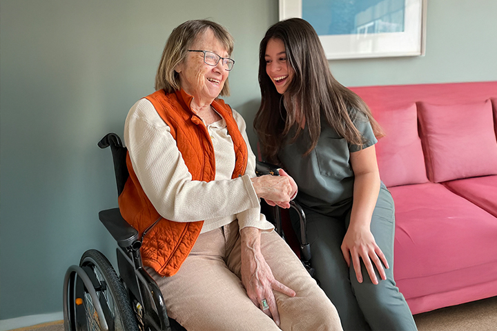 Smiling elderly woman in a wheelchair shaking hands with a happy caregiver in a living room.