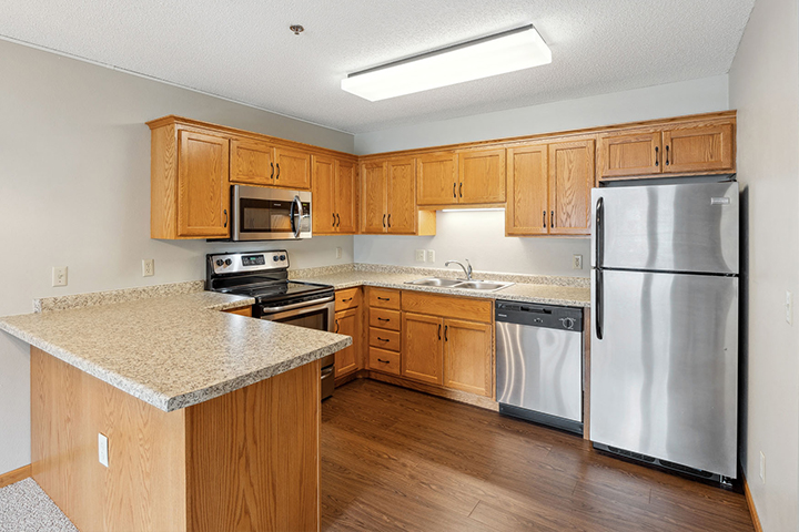 Modern kitchen with wood cabinets, stainless steel appliances, and a large countertop under bright lighting.