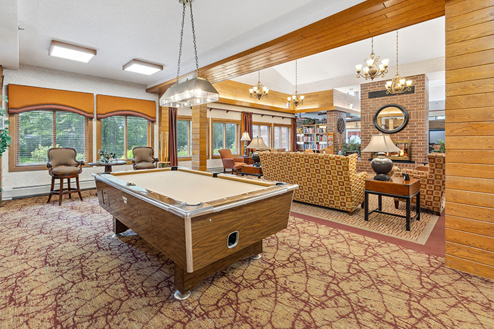 Spacious lounge area with a pool table, cozy seating, large windows, and warm lighting fixtures.