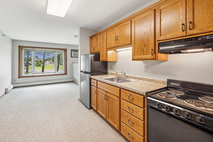 Assisted living kitchen with wood cabinets, electric stove, and window overlooking a grassy outdoor area.