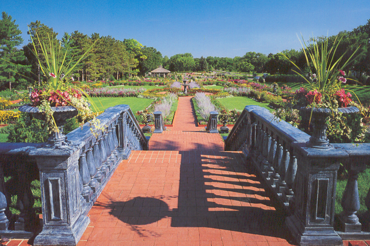Stone steps lead to vibrant Musinger Clemens Gardens, with flowers, greenery, and a gazebo in the distance.