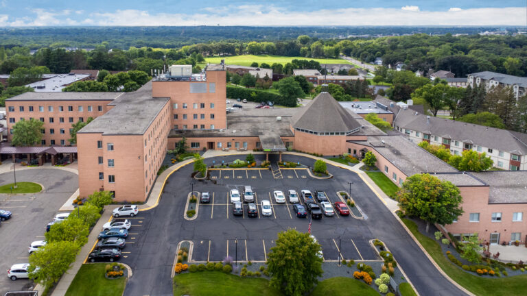 Aerial view of a large brick building with a parking lot and surrounding greenery.