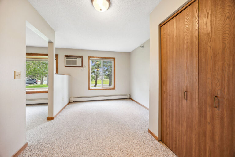 Benedict Court bedroom with beige carpet, wooden closet doors, and a window with a view of trees and grass outside.