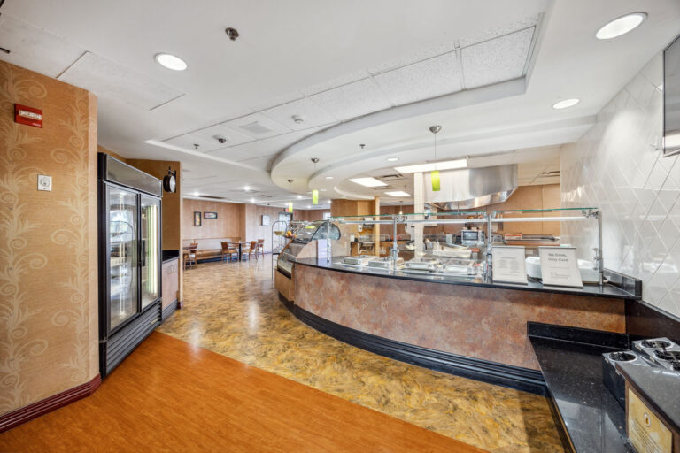 Spacious bistro with buffet-style serving area, empty seating, tiled floor, and ceiling lights.