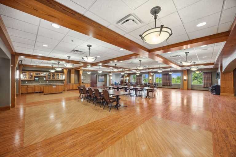 Bonn Great Room: A spacious dining hall with wooden floors, tables, chairs, pendant lights, and art-adorned walls.
