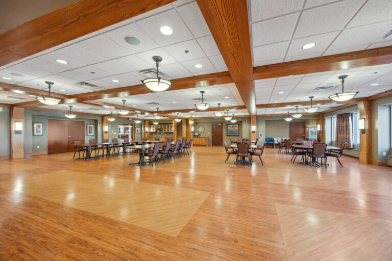 Bonn Great Room: A spacious dining hall with wooden floors, tables, chairs, pendant lights, and art-adorned walls.