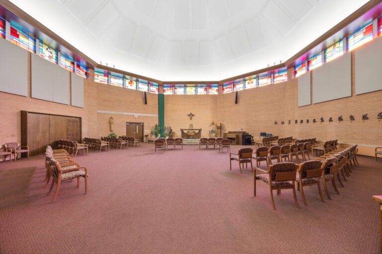 The Main Chapel boasts a spacious auditorium with wooden chairs, stained glass windows, and a brown carpet.