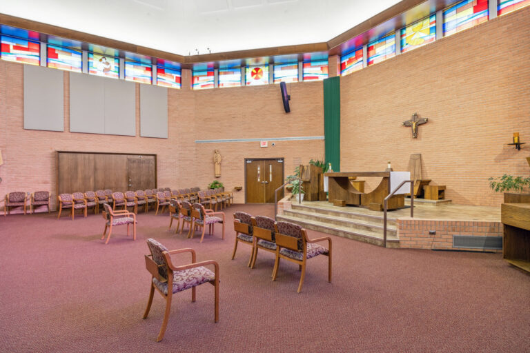 The main chapel boasts chairs, stained glass windows, a cross, and an altar on a raised platform.