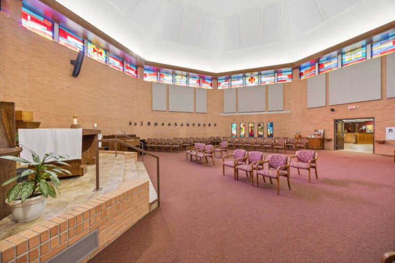 The Main Chapel boasts a spacious auditorium with wooden chairs, stained glass windows, and a brown carpet.