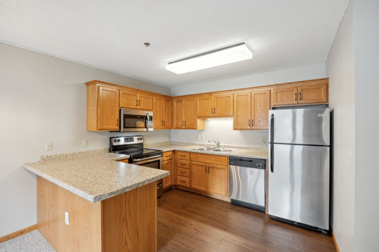 Benedict Village Apartment kitchen with wooden cabinets, black appliances, and a marble-pattern countertop under overhead light.