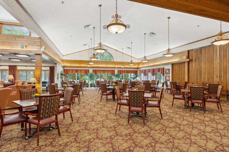 Spacious dining room with wooden chairs, tables, large windows, patterned carpet, and decorative ceiling lights.
