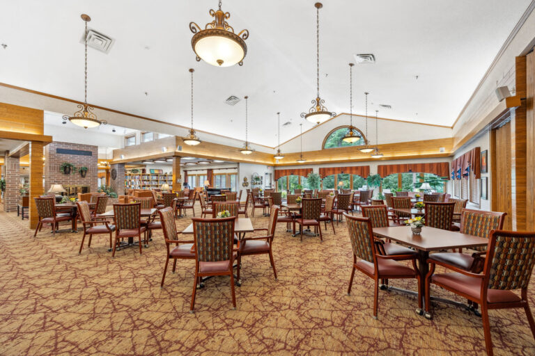 Spacious dining room with wooden chairs, tables, large windows, patterned carpet, and decorative ceiling lights.