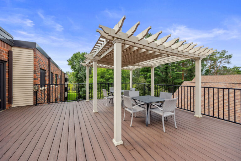 Benedict Village Rooftop Terrace boasts a pergola, table, and chairs, all framed by a black railing under a clear blue sky.