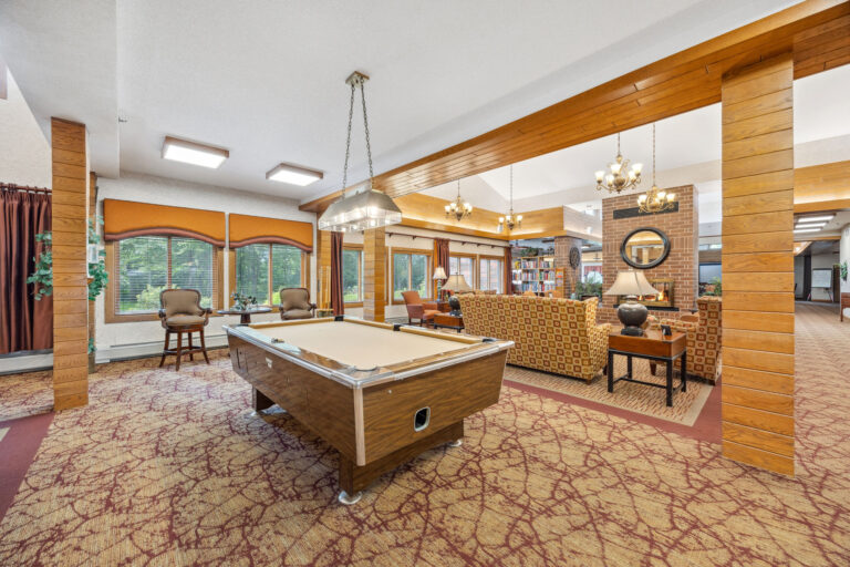 Benedict Villages recreational room features a pool table, lounge chairs, bookshelves, and garden-view windows.