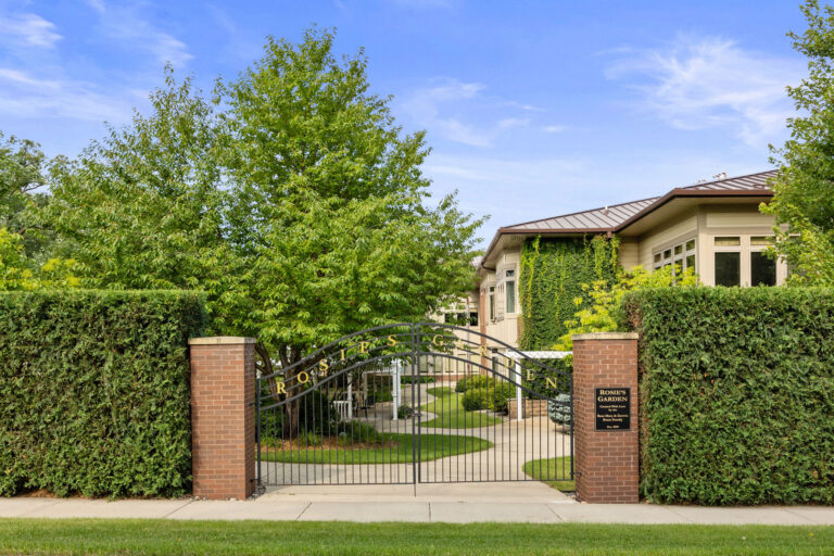 Gated entrance to Rosies Garden, surrounded by lush greenery and a pathway leading to a building.