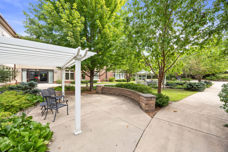 Rosies Garden Seating Area features an outdoor patio with chairs under a pergola amidst lush trees and greenery.