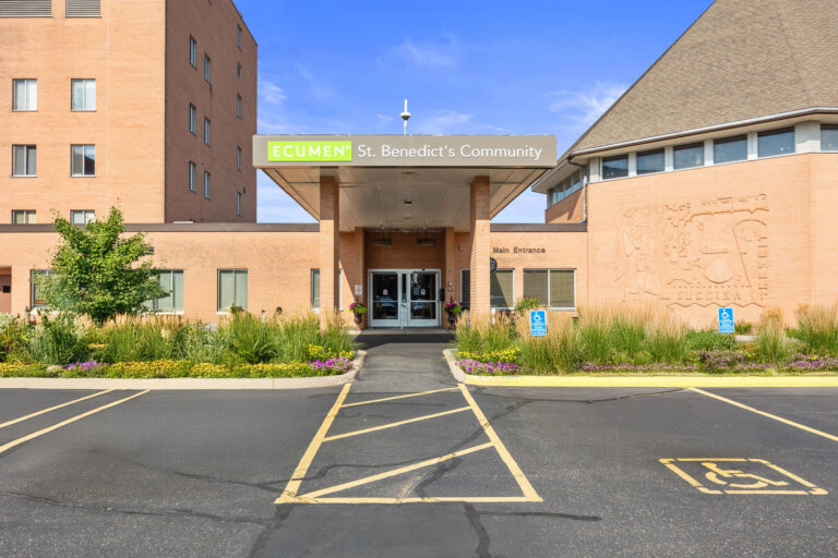 Main entrance of Ecumen St. Benedicts Community building with accessible parking and landscaped greenery.