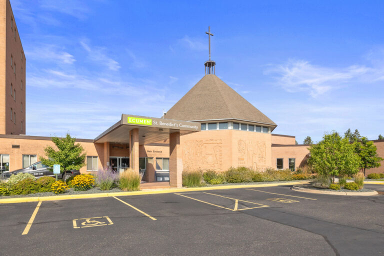 Main entrance of Ecumen St. Benedicts Community building with accessible parking and landscaped greenery.
